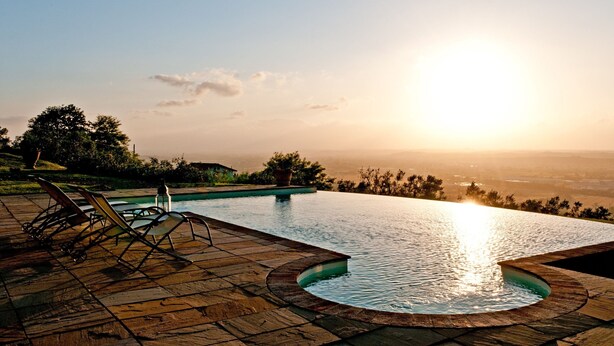 Ein Infinity-Pool mit Blick auf den Sonnenuntergang, Liegestühle und eine Steinterrasse.