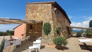 Ein Steinhaus mit einer Terrassenfläche, die weiße Möbel und eine Pergola zeigt.