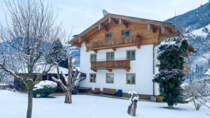 Un chalet en bois à deux étages, doté de balcons, entouré d’arbres couverts de neige et avec des montagnes en toile de fond.
