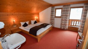 Une chambre dans un chalet en bois, avec un lit, une table de chevet, un lavabo et une fenêtre avec des rideaux.