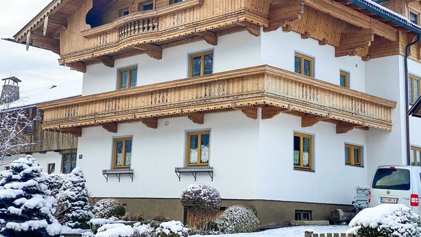 Un immeuble en bois à plusieurs étages, doté de balcons, avec une voiture garée devant et de la neige au sol.