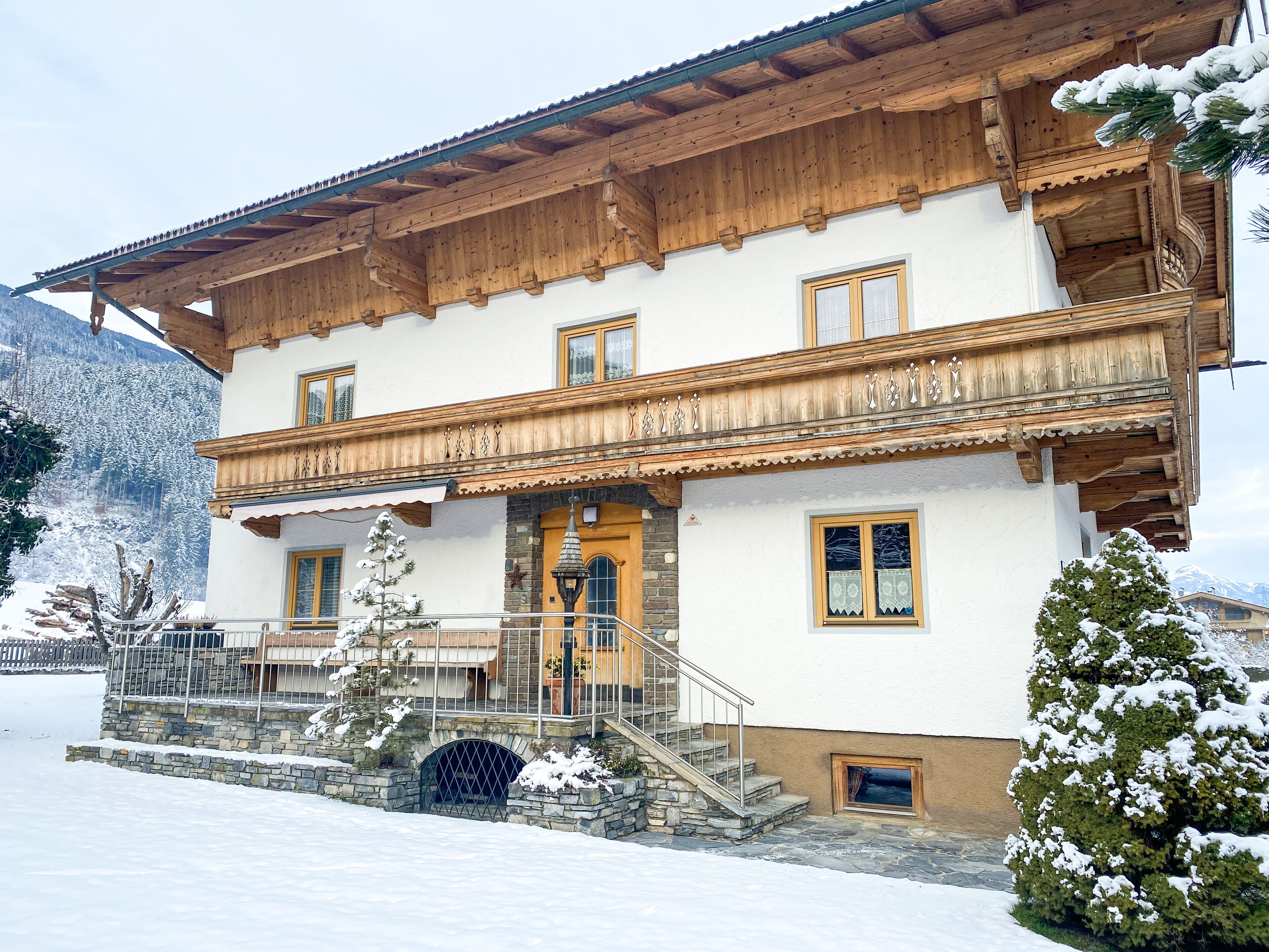 Een klassiek chalet met een houten balkon, stenen trappen en een besneeuwde omgeving.