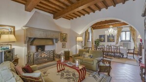 A spacious living room with a fireplace, wooden beams, a dining area, and a chandelier. - Belvilla by OYO Villa Terra (Reggello)