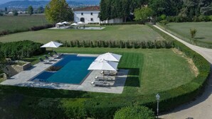 A large swimming pool with sun loungers and umbrellas, surrounded by well-manicured lawns and a white building in the background. - Belvilla by OYO Villa Terra (Reggello)
