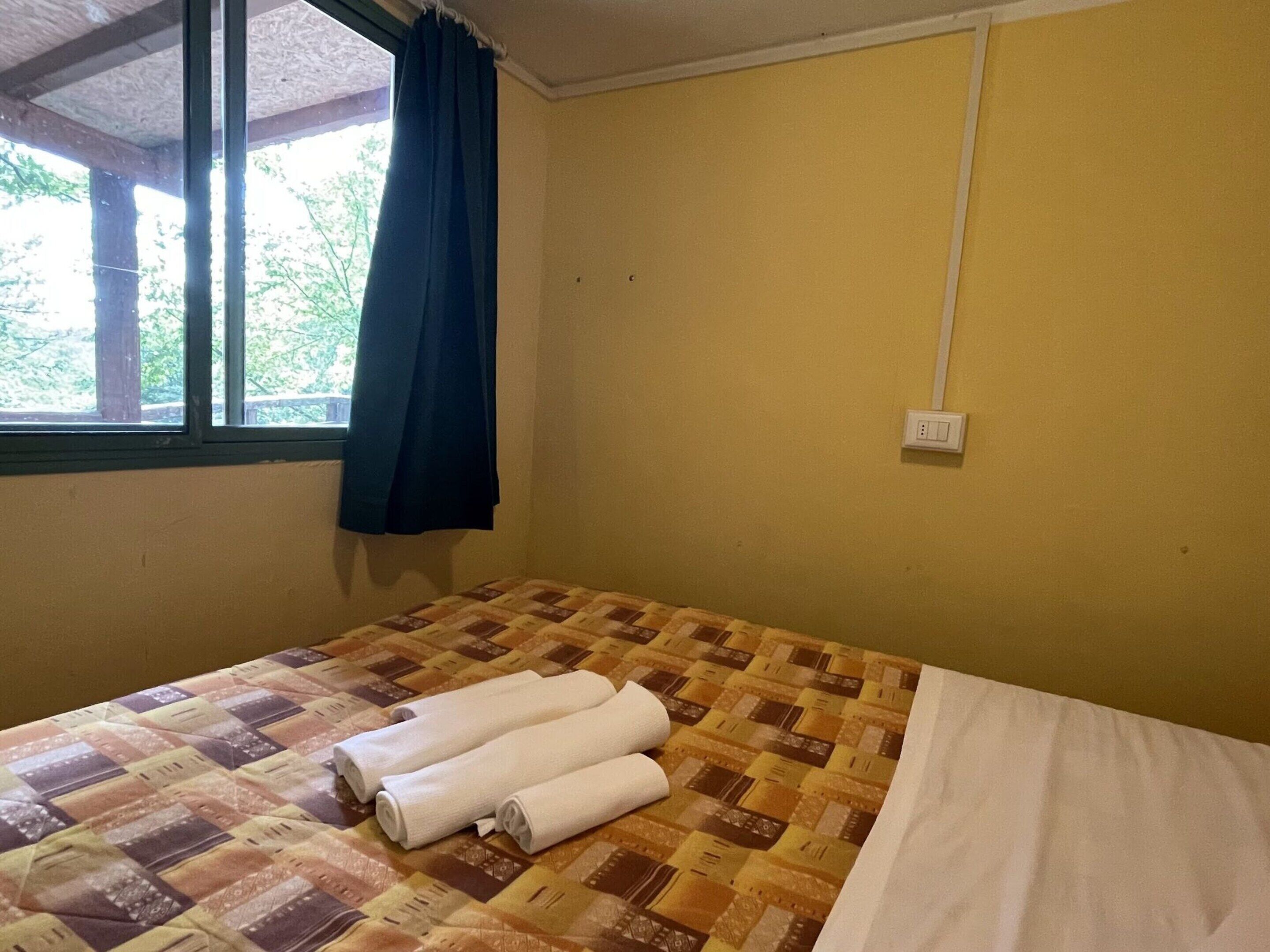 A room with a bed, a window with curtains, and a wall socket.