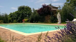 Una piscina con una estatua, rodeada de exuberante follaje y un cielo despejado.