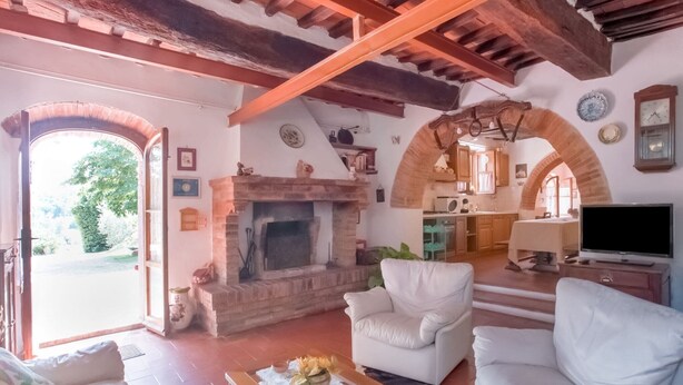 Un salón amplio con chimenea, sofás blancos, televisor y una cocina abierta al fondo.