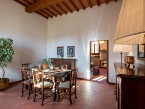 A dining area with a wooden table and chairs, a potted plant, and a view into the kitchen.