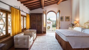 A spacious bedroom with a large bed, a seating area with two chairs, a wooden wardrobe, and a view through an open door to the outside. - Belvilla by OYO Villa Iole (Reggello)