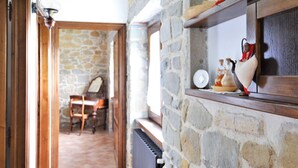 Un mur en pierre avec une étagère où sont disposés des objets décoratifs, une chaise et une table à l’arrière-plan.