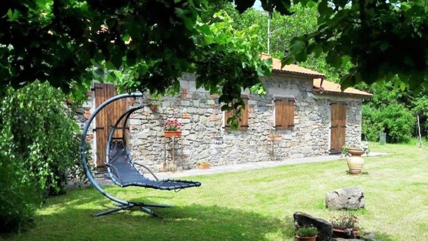 Une maison en pierre avec un jardin, une chaise suspendue et une petite table.