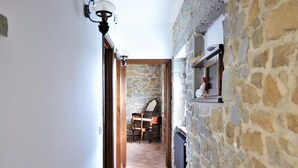 Un couloir étroit, avec un mur en pierre et un sol carrelé, qui mène à une pièce contenant une chaise en bois et une table.