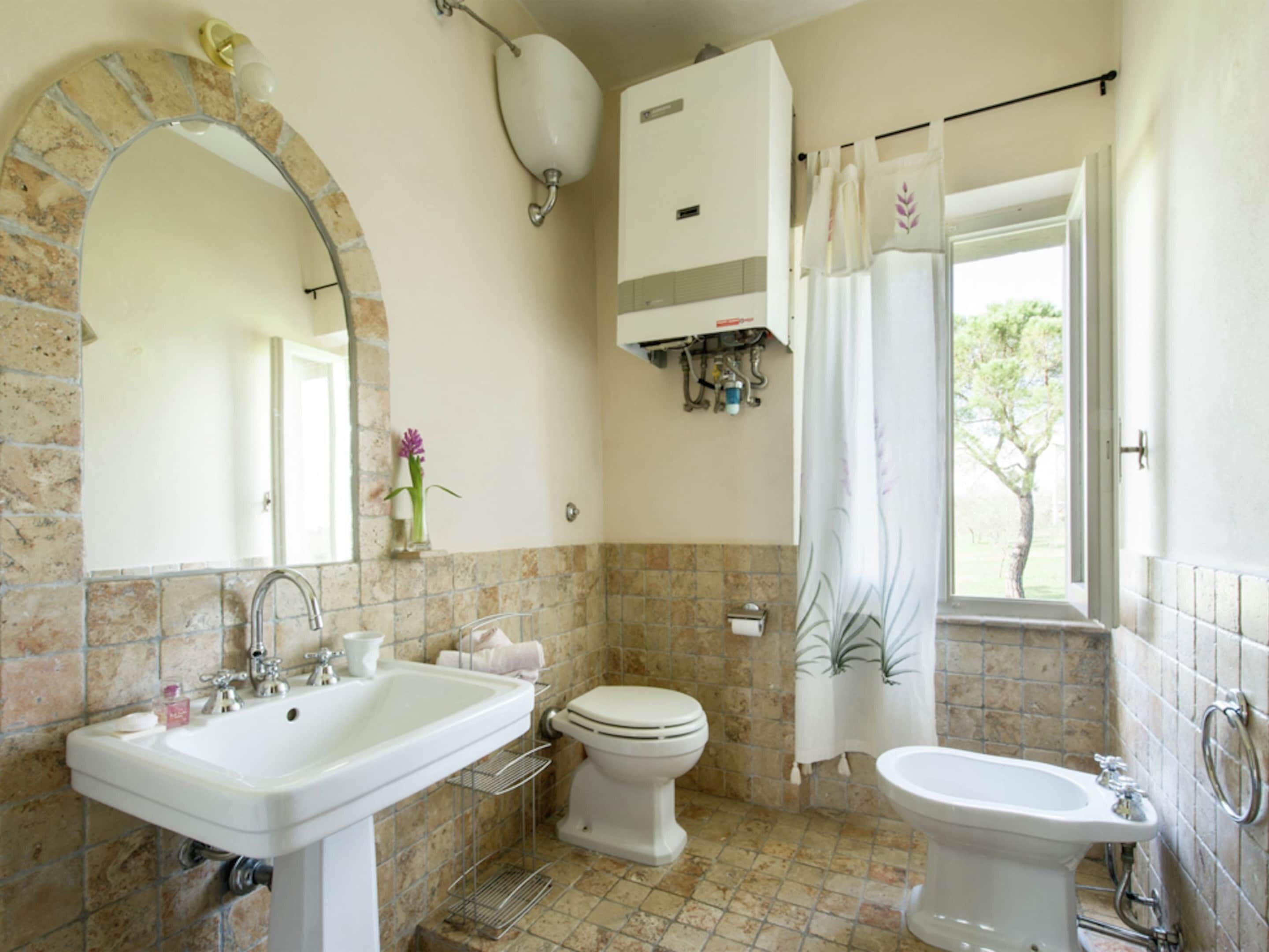 Een badkamer met een wastafel, toilet en bad. Er is een spiegel met een stenen lijst, een handdoekhouder en een douchegordijn.