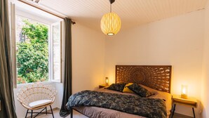 A bedroom with a bed, a chair, a window with curtains, a wooden headboard, and two bedside lamps. - MAS SAINT LAURENT (Les Salles-du-Gardon)