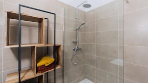 A shower area with a glass door, a metal showerhead, and wooden shelves with towels. - MAS SAINT LAURENT (Les Salles-du-Gardon)