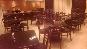 Une salle à manger d’hôtel avec plusieurs tables et chaises, un espace cuisine équipé d’appareils électroménagers et un comptoir.