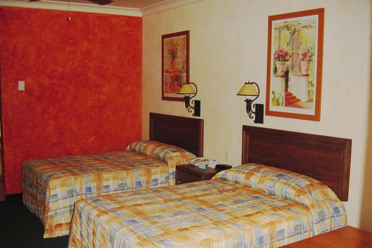 Habitación de hotel con dos camas, una pared roja y dos lámparas fijadas a la pared.