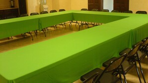 Une salle de conférence avec une longue table recouverte d’une nappe verte, entourée de chaises.