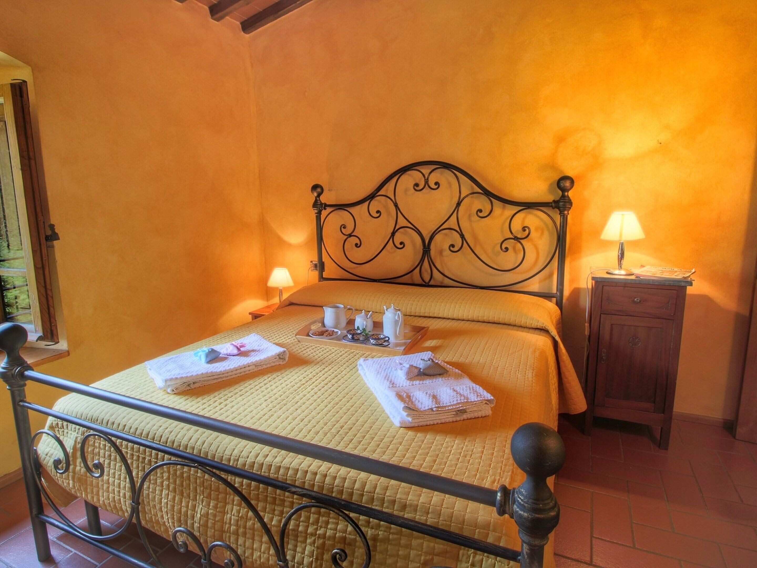 A bed with a metal frame, a bedside table with a lamp, and a window with a view of greenery.
