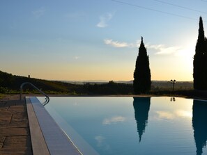 A swimming pool with a clear view of the surrounding landscape, including distant hills and tall cypress trees.