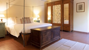 Quarto com cama de dossel, um guarda-roupa de madeira e mesa de cabeceira com abajur.
