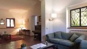 Uma sala de estar com sofá, mesa de centro, piano e janela com grades decorativas de ferro.