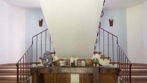 Uma escadaria com corrimão de madeira e guarda-corpo de metal, que leva a um patamar com um vaso decorativo e uma pequena mesa.