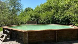 Uma banheira de hidromassagem de madeira retangular com escada em um deck de madeira, rodeada por vegetação exuberante.