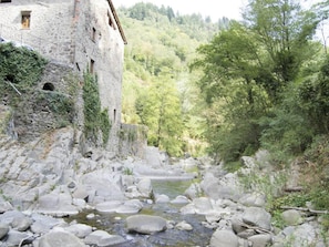 A stone building with a rustic appearance, a narrow stream with rocks, and a forested hillside in the background. - Charming Mill by Pescia River w/ Garden (Pescia)