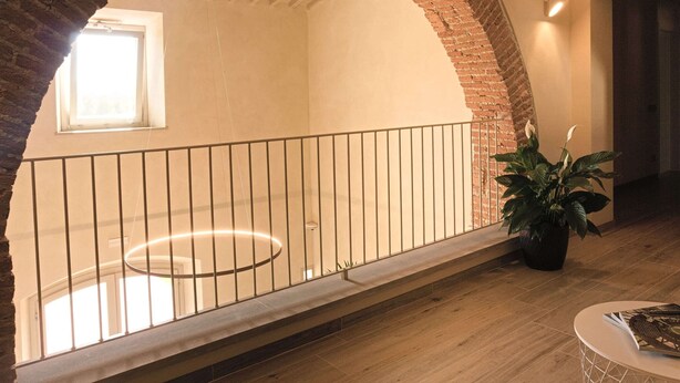 Een ruim interieur met een hoge plafond, een bakstenen boog, een balkon met leuning en een plant in pot.