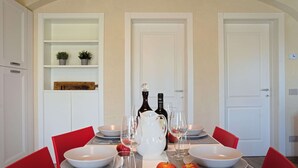 Een eettafel gedekt met borden, glazen en appels, met een witte kast en een deur op de achtergrond.