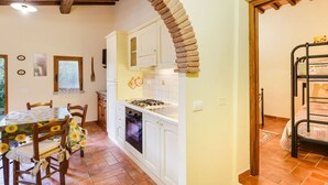 Una cucina con mobili bianchi, zoccolo in piastrelle e arco in mattoni.