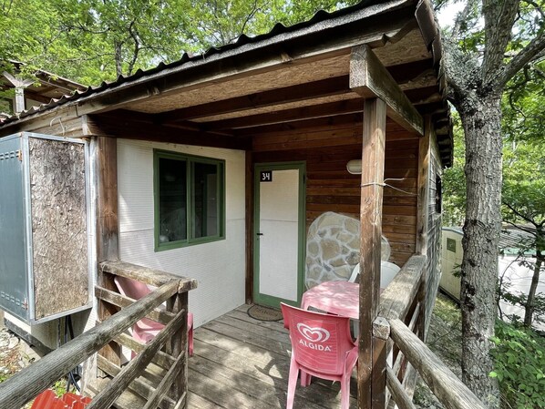 A rustic cabin with a wooden porch, a stone wall, and a door marked with the number 34.