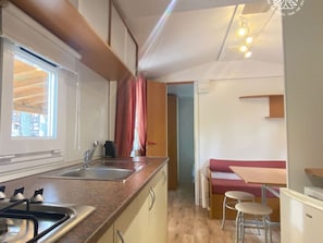 A compact kitchen with a sink, stove, and wooden cabinets. There is a dining area with a bench and stools.