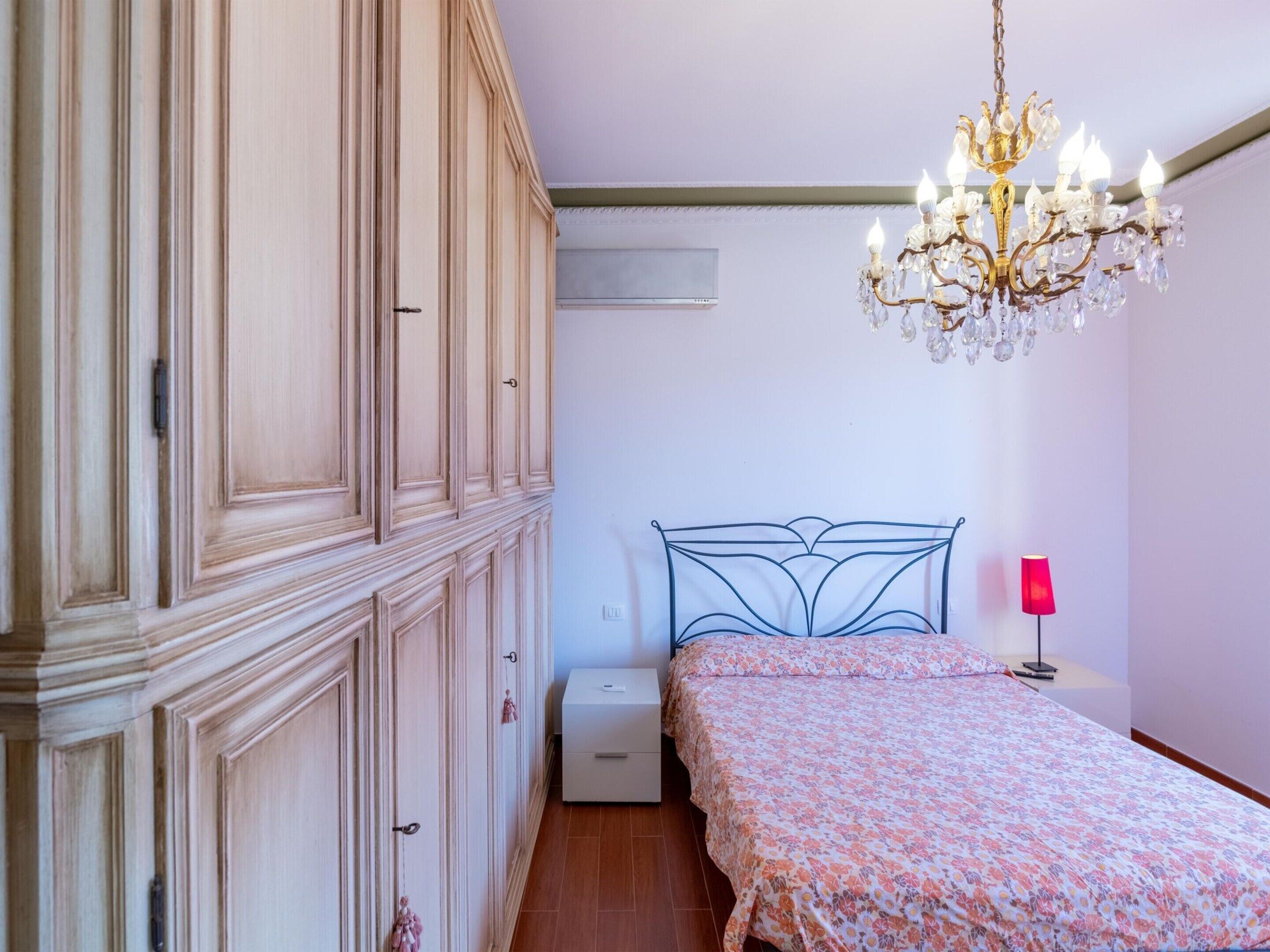 A bedroom with a bed, a dresser, a nightstand, a chandelier, and an air conditioning unit.