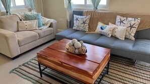 Een woonkamer met een beige bank, een grijze bank en een houten salontafel met decoratieve objecten.