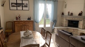 Una sala de estar acogedora con chimenea, una mesa de comedor con un centro de mesa floral y una cortina azul.