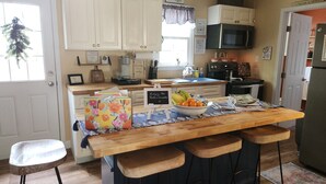 A kitchen with a central island, bar stools, a refrigerator, and various kitchen appliances. - Cozy Guest House on 15 acres, with plenty of parking! (Parsonsburg)