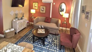 A living room with a sofa, armchair, coffee table, and a flat-screen TV mounted on the wall. - Cozy Guest House on 15 acres, with plenty of parking! (Parsonsburg)