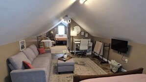 A cozy attic bedroom with a bed, a sofa, a desk, and a TV. - Cozy Guest House on 15 acres, with plenty of parking! (Parsonsburg)