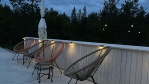 Un espace extérieur aménagé en terrasse, avec des chaises et une table en osier, entouré d’une plateforme en bois et d’une balustrade blanche.