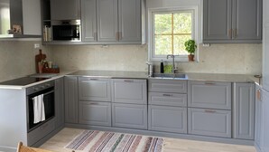 Une cuisine moderne avec des meubles gris, un four encastré, un four à micro-ondes et une fenêtre donnant sur un espace verdoyant.