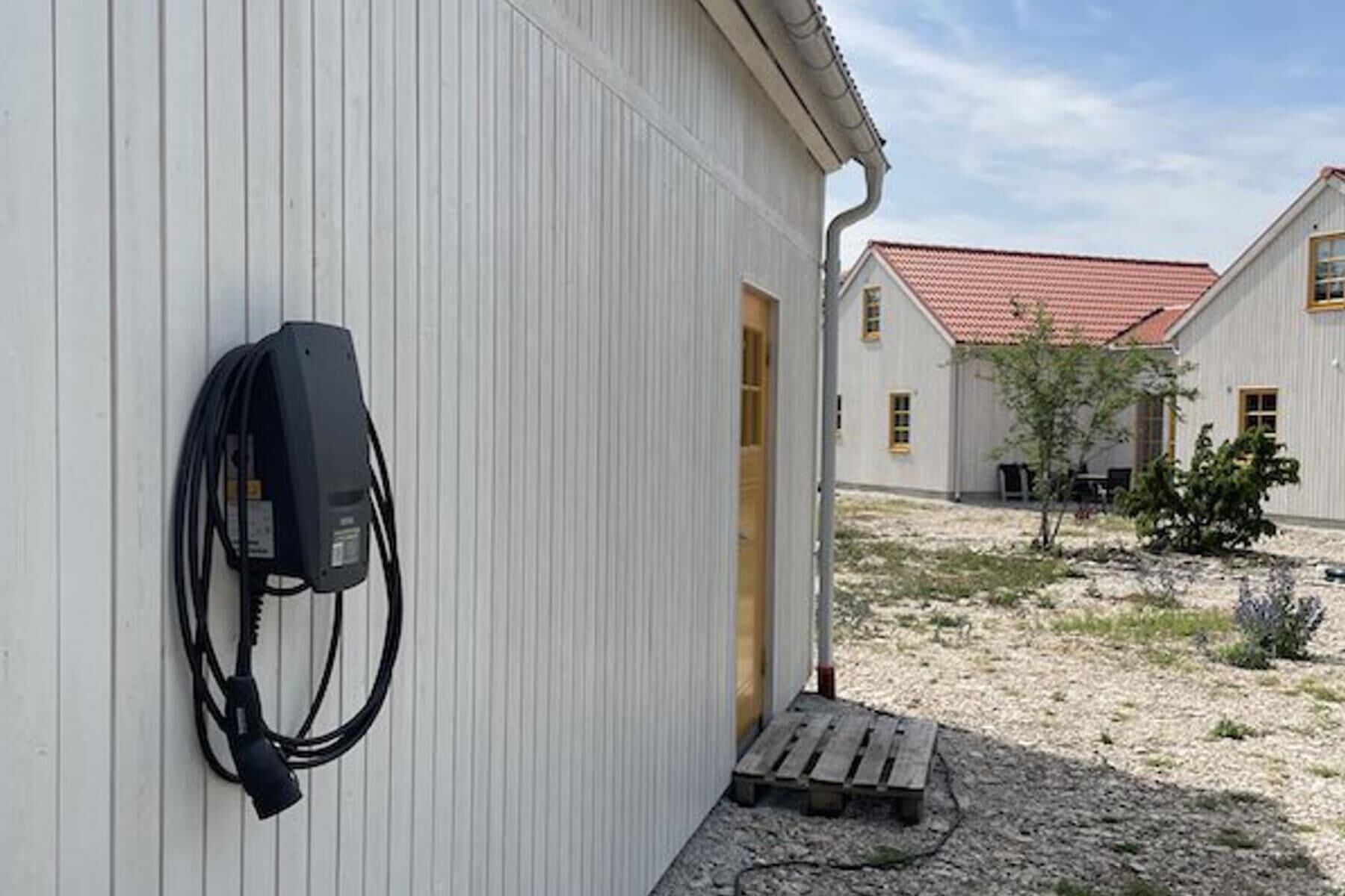 Un bâtiment à l’extérieur blanc et au toit rouge. On y voit une boîte électrique noire fixée au mur et une porte en bois donnant sur l’intérieur.