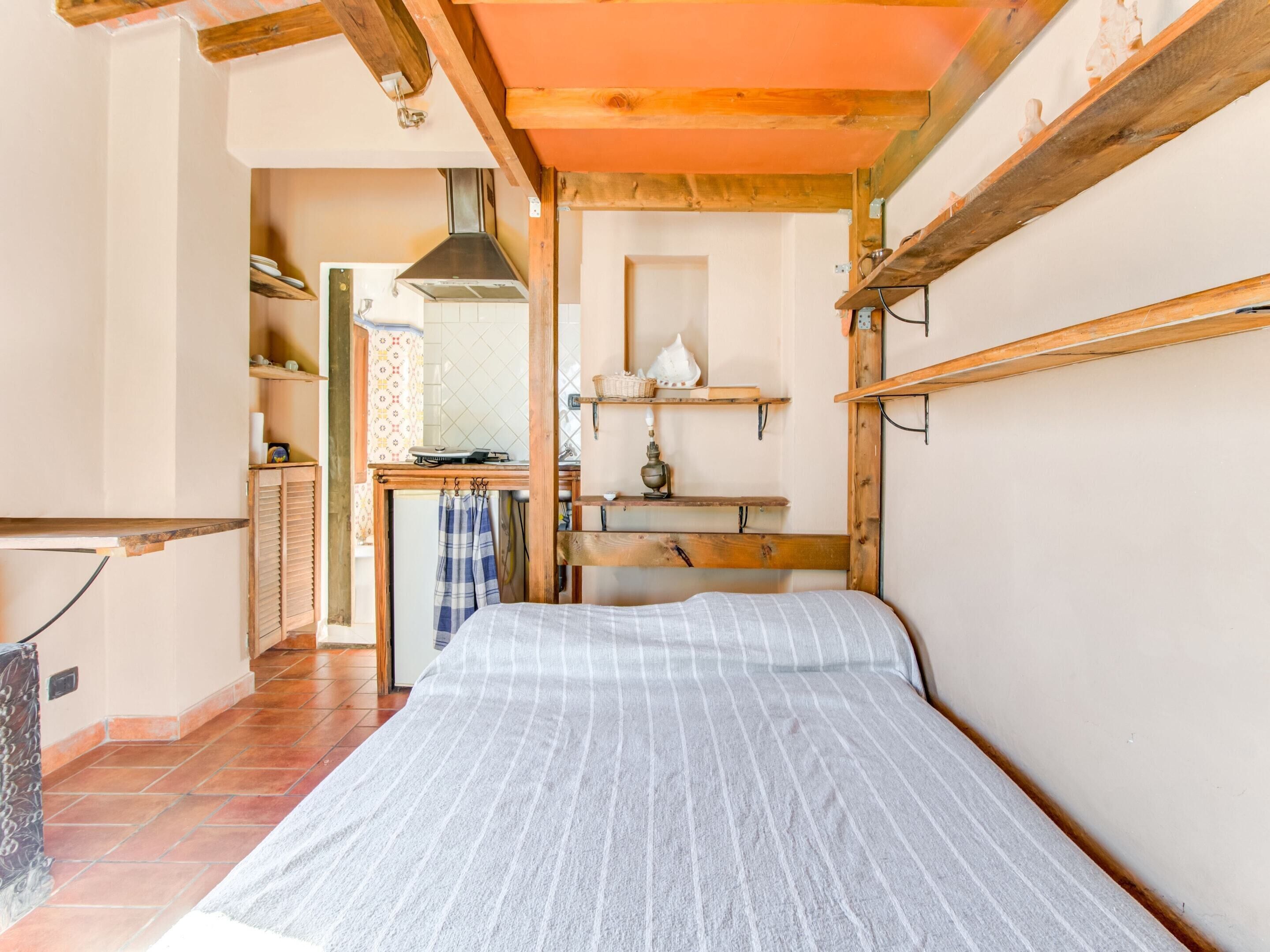 Un dormitorio acogedor con cama, vigas de madera, una kitchenette pequeña y un baño.
