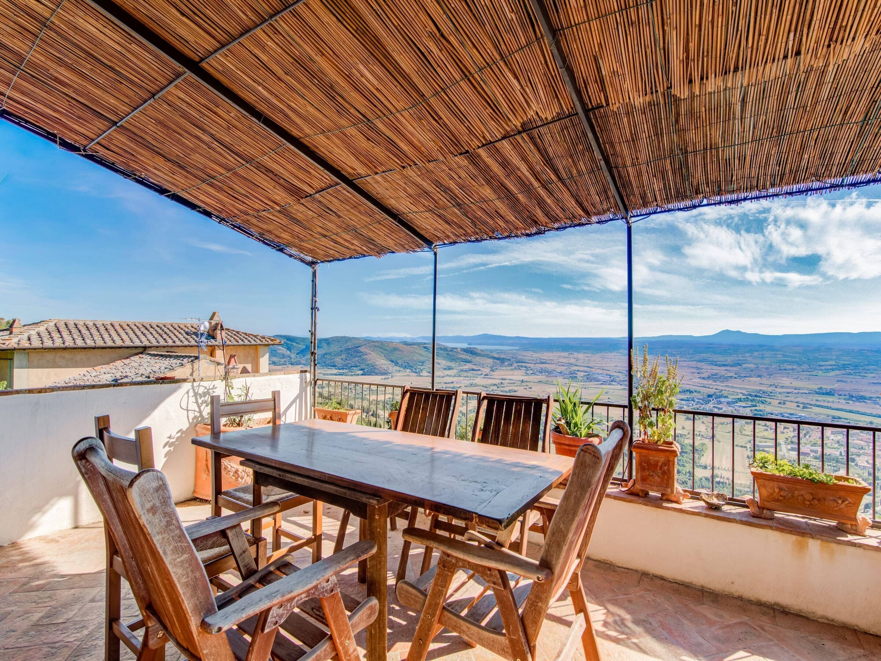 Una terraza con mesa y sillas, plantas en macetas y vistas a colinas distantes.