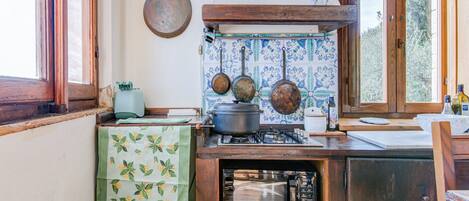 A kitchen with a stove, microwave, hanging pots, and a window with a view of greenery.