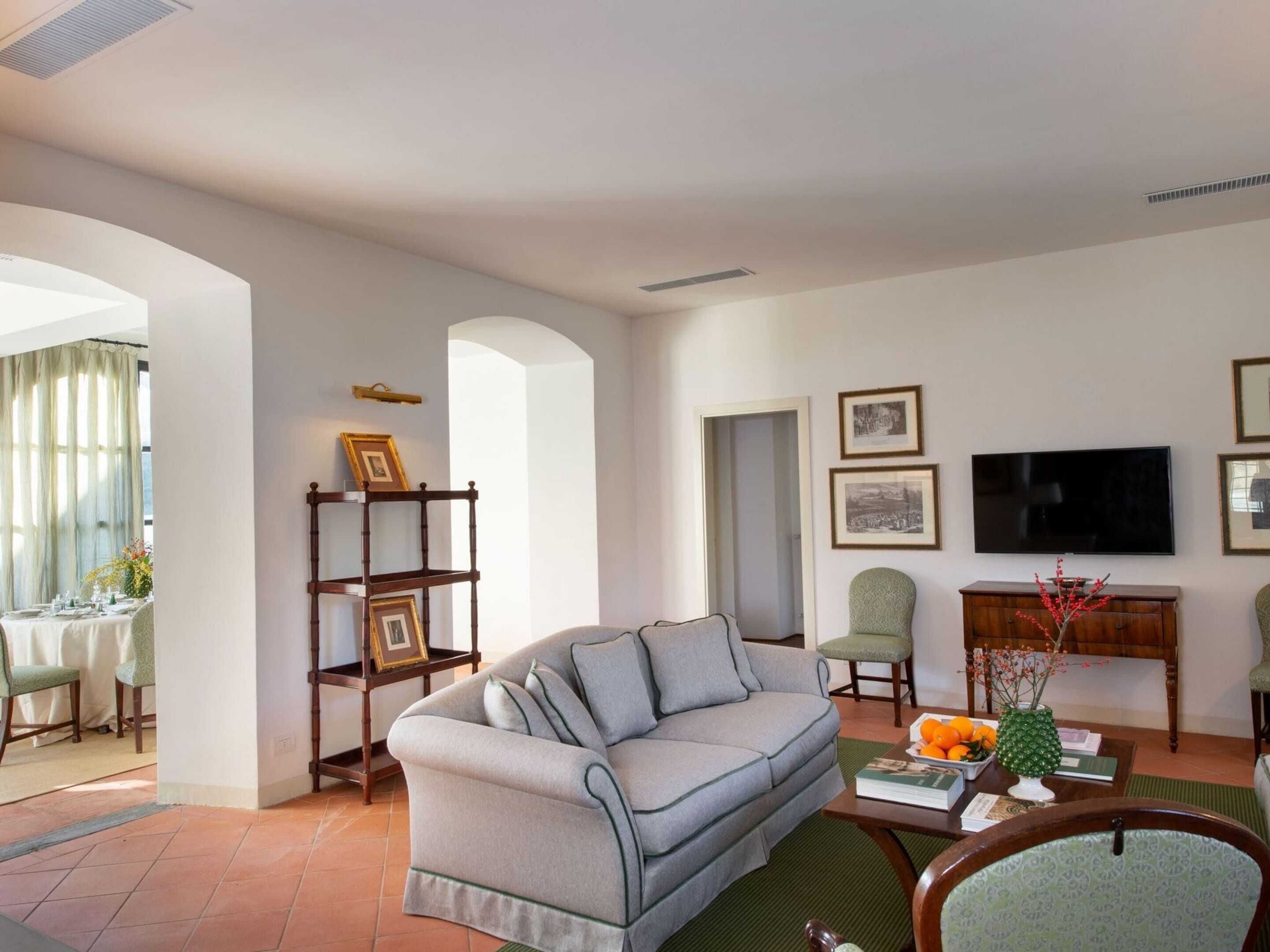 Una sala de estar con un sofá gris, una mesa de centro con libros y un florero, un televisor y cuadros en la pared.