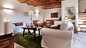 A cozy living room with a brick ceiling, white walls, and a green rug. There are two white sofas, a wooden coffee table, and a lamp. A map and books are on the shelves. - Villa in Chianti With Pool & Tennis Court (Gaiole in Chianti)