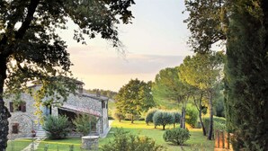 A stone building with a garden in front, surrounded by trees and a clear sky. - Villa in Chianti With Pool & Tennis Court (Gaiole in Chianti)