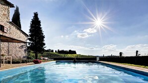 A swimming pool with clear water, surrounded by stone buildings and a hedge. - Villa in Chianti With Pool & Tennis Court (Gaiole in Chianti)